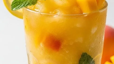 Refreshing frozen mango peach lemonade in a glass with ice and fruit garnish