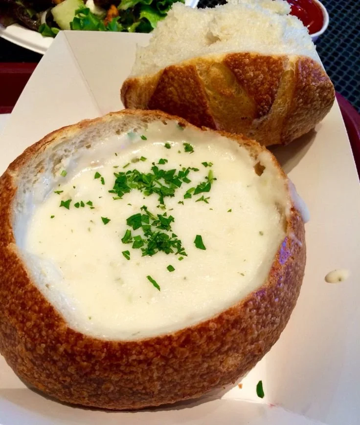 Delicious bowl of clam chowder topped with herbs and served with bread