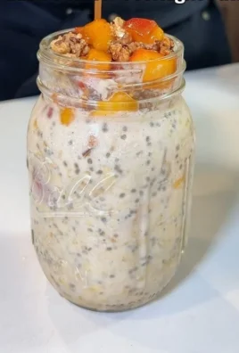 Creamy peach cobbler overnight oats in a glass jar with fresh peaches.
