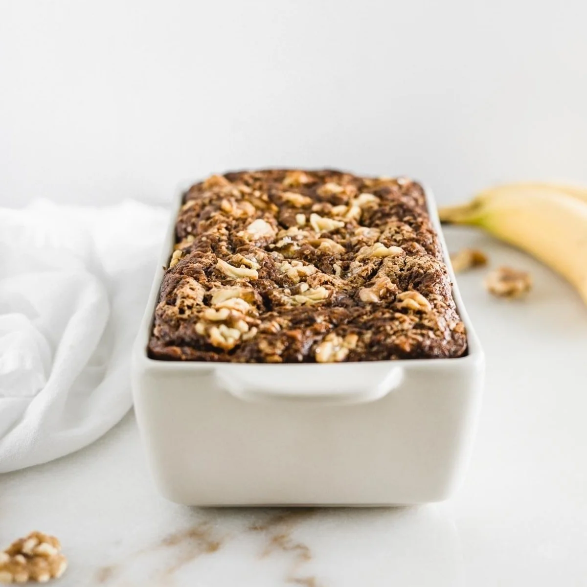 Healthy banana nut bread with walnuts and ripe bananas on a wooden table.