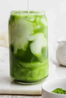 Iced Matcha Latte in a glass with ice and matcha powder on the side