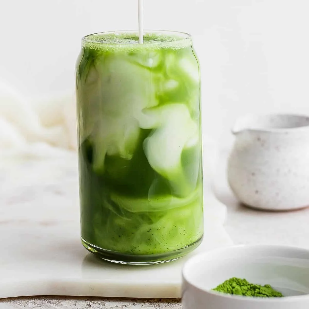 Iced Matcha Latte in a glass with ice and matcha powder on the side