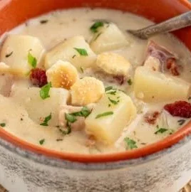 Bowl of New England clam chowder topped with fresh parsley and served with crackers.