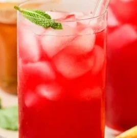 Glass of refreshing Honey Hibiscus Lemonade with lemon and hibiscus flowers.