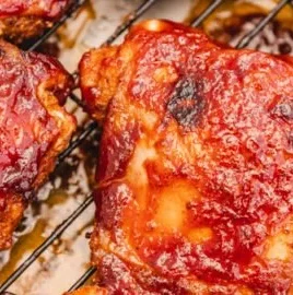 Baked BBQ chicken thighs ready to serve with sauce and sides.