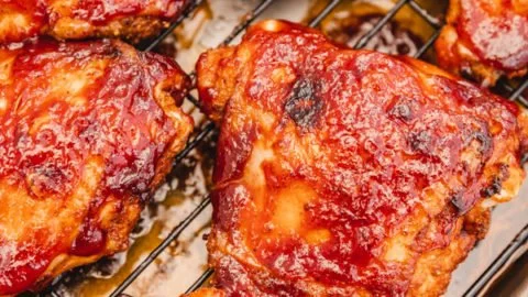 Baked BBQ chicken thighs ready to serve with sauce and sides.