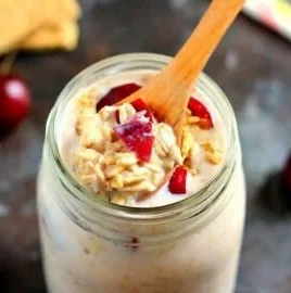 Bowl of cherry pie overnight oats topped with fresh cherries and cream