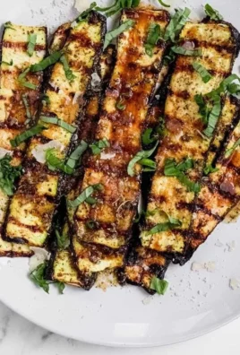 Grilled zucchini topped with melted parmesan cheese on a serving platter.