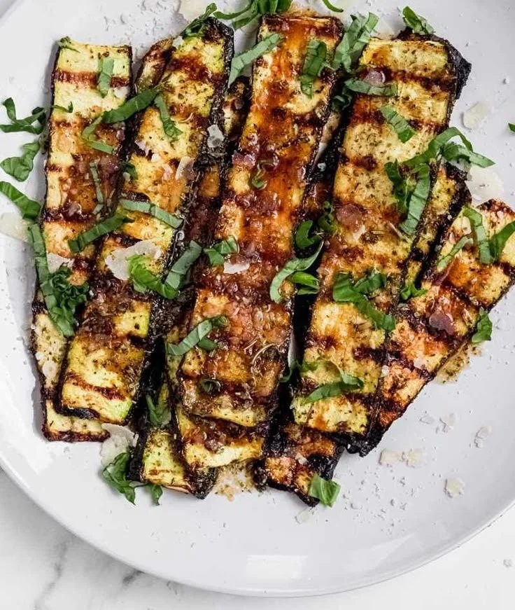 Grilled zucchini topped with melted parmesan cheese on a serving platter.