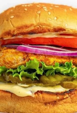 Juicy grilled chicken sandwich on a plate with lettuce and tomato.